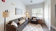 Located at 4000 E River Rd in West Henrietta, NY, this single-floor unit offers a well-organized layout designed for comfortable shared or individual living. The open-concept kitchen is outfitted with white cabinetry, granite-style countertops, black appliances including a range, microwave, and dishwasher, and a peninsula with a stainless steel sink that flows naturally into the dining and living areas. The living room features wood-look flooring, a large window that invites natural light and outdoor views, and ample space for seating. Multiple bedrooms are carpeted and each includes a window overlooking greenery, providing a bright and private retreat. Each bedroom also features dedicated closet space, and several rooms accommodate a desk and chair, making them well-suited for study or work. The unit includes multiple full bathrooms, each finished with white vanity cabinetry, a single sink with mirror, tile flooring, and a shower/tub combination. The overall aesthetic throughout the unit is clean and neutral, with light gray and white tones creating a cohesive, modern feel across all rooms.