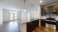 This well-appointed single-floor residence combines contemporary design with functional living spaces, offering a cohesive and inviting atmosphere throughout. The open-concept kitchen is a standout feature, showcasing rich dark cabinetry, granite countertops, a subway tile backsplash, and a full suite of stainless steel appliances including a refrigerator, range, and microwave. A large central island with an integrated sink and pendant lighting above serves as both a workspace and a natural gathering point, flowing seamlessly into the living area with warm hardwood-style flooring. A sliding barn door adds a modern architectural touch to the transition between the living space and the bedrooms. The bedrooms are generously sized, each featuring plush carpeting, ceiling fans, and multiple windows dressed with blinds that invite ample natural light and outdoor views. The bathrooms are finished with granite vanity tops, dark cabinetry with brushed nickel hardware, and hardwood-style flooring, with the primary bath offering a dual-sink vanity. Throughout the residence, a neutral color palette, clean lines, and quality finishes create a bright, modern, and comfortable living environment.