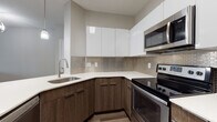 This single-floor residence showcases a thoughtfully designed layout with contemporary finishes throughout. The kitchen is a standout feature, boasting two-tone cabinetry with dark wood lower cabinets and high-gloss white upper cabinets, complemented by light quartz countertops and a neutral mosaic tile backsplash. Stainless steel appliances, including a refrigerator, electric range, and over-the-range microwave, complete the space. A peninsula provides additional counter space and casual seating, while wood-look flooring ties the kitchen seamlessly into the open living area.

The living room is anchored by a classic fireplace with a crisp white mantel, adding warmth and character to the neutral, light-toned space. Pendant lighting and wood-look flooring contribute to the modern aesthetic throughout the common areas.

The bedrooms are finished with plush carpeting and feature natural light from multiple windows dressed with horizontal blinds. Each bedroom offers closet storage, including a walk-in closet option, providing generous organizational space.

The bathroom is tastefully designed with wood-plank-style floor tile and a matching tile surround in the tub-shower combination, paired with a dark wood vanity and white countertop for a cohesive, modern look throughout.
