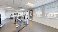 Located in Draper, Utah, this fitness center offers a comprehensive workout facility designed to support a wide range of exercise routines. The space is contained on a single floor and provides a generous, open layout that accommodates multiple workout zones without feeling crowded.

The room features durable rubber flooring throughout, ideal for both cardio and strength training activities. A row of treadmills lines one wall, accompanied by a wall-mounted flat-screen television, making cardio sessions more engaging. Multiple Matrix-brand cycling bikes occupy a central area of the room, offering dedicated space for spin workouts. Additional cardio equipment, including elliptical machines and upright bikes, is distributed throughout the space.

A free weights section provides medicine balls and a weight rack, supporting varied strength training needs. A large wood-framed mirror is mounted on one wall, enhancing both functionality and the sense of openness. A water cooler station is conveniently positioned nearby for easy hydration access.

Multiple windows fitted with horizontal blinds allow natural light to fill the space while maintaining privacy. Recessed drop-ceiling panels with integrated fluorescent lighting ensure consistent illumination throughout. A glass-panel exterior door provides direct outdoor access. The clean white walls and bright, neutral aesthetic contribute to an energizing and focused workout environment.