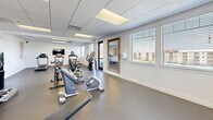 Located in Draper, Utah, this fitness center offers a comprehensive workout facility designed to support a wide range of exercise routines. The space is contained on a single floor and provides a generous, open layout that accommodates multiple workout zones without feeling crowded.

The room features durable rubber flooring throughout, ideal for both cardio and strength training activities. A row of treadmills lines one wall, accompanied by a wall-mounted flat-screen television, making cardio sessions more engaging. Multiple Matrix-brand cycling bikes occupy a central area of the room, offering dedicated space for spin workouts. Additional cardio equipment, including elliptical machines and upright bikes, is distributed throughout the space.

A free weights section provides medicine balls and a weight rack, supporting varied strength training needs. A large wood-framed mirror is mounted on one wall, enhancing both functionality and the sense of openness. A water cooler station is conveniently positioned nearby for easy hydration access.

Multiple windows fitted with horizontal blinds allow natural light to fill the space while maintaining privacy. Recessed drop-ceiling panels with integrated fluorescent lighting ensure consistent illumination throughout. A glass-panel exterior door provides direct outdoor access. The clean white walls and bright, neutral aesthetic contribute to an energizing and focused workout environment.