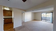 This single-floor unit offers a practical and well-organized layout designed for comfortable everyday living. The main living area is generously sized, featuring neutral-toned carpet flooring, a textured ceiling, and a ceiling fan overhead. A structural beam adds subtle architectural definition to the space, while a sliding glass door along one wall opens to an outdoor balcony, allowing natural light to filter in. Adjacent to the living area, the kitchen is equipped with dark wood cabinetry, dark granite-style countertops, a double stainless steel sink, and white appliances including an electric range and refrigerator. The kitchen's peninsula-style counter provides a convenient pass-through to the living space. The bedrooms are carpeted and feature neutral walls, textured ceilings, and windows with vertical blinds that bring in natural light and outdoor views. Each room offers a clean, versatile canvas. The bathrooms are fitted with dark granite-style countertops, wood-toned vanity cabinetry, full-width mirrors, and overhead vanity lighting. The unit also features hardwood-style flooring in the entryway and kitchen areas, providing a pleasant contrast to the carpeted rooms throughout the rest of the space.