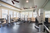 Located at 2311 Ivy Hill Way in San Ramon, California, this fitness center offers a well-appointed, single-floor exercise facility designed to support a comprehensive workout experience. The space is thoughtfully laid out across one open room, making efficient use of its footprint to accommodate a wide variety of equipment.

The gym is lined with large windows fitted with horizontal blinds along multiple walls, flooding the interior with natural light and offering views of the surrounding outdoor amenity areas, including a glimpse of a pool and landscaping. A glass door provides direct outdoor access, further enhancing the open, airy feel of the space.

The tray-style ceiling features recessed lighting and multiple ceiling fans, ensuring consistent airflow and a comfortable environment during workouts. Durable rubber flooring covers the entire exercise area, providing cushioning and slip resistance throughout.

Equipment is well-distributed across the space, including a selection of cardio machines such as treadmills, ellipticals, and a stationary bike, as well as a variety of strength training stations, cable machines, adjustable benches, and a dumbbell rack. A wall-mounted flat-screen television is positioned near the cardio section for entertainment. Full-length mirrors on one wall enhance the sense of space and allow users to monitor their form. The overall ambiance is clean, functional, and well-maintained.