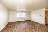 This single-floor unit offers a practical and well-organized layout designed for comfortable everyday living. The main living area is generously proportioned, featuring rich wood-look laminate flooring, crisp white walls, and a textured ceiling. A large sliding window allows natural light to fill the space, creating a bright and open atmosphere. A floor vent provides in-unit climate control, while a thermostat on the wall adds convenience.

The galley-style kitchen runs along two parallel walls, offering abundant warm oak cabinetry for storage above and below the counters. Light-toned laminate countertops provide ample workspace, and the kitchen is equipped with black appliances, including a refrigerator and range, as well as a stainless steel sink and dishwasher. The wood-look flooring continues seamlessly from the main living area into the kitchen.

Two bedrooms are finished with plush wall-to-wall carpeting and feature large windows fitted with blinds, allowing for natural light while maintaining privacy. At least one bedroom includes a dedicated closet with a clothing rod for organized storage.

The full bathroom is accessible off the main hall and features wood-look flooring, a tub and shower combination with white tile surround, a toilet, and a vanity with cabinet storage. Warm wood-toned doors and trim are consistent throughout, lending a cohesive and tidy character to the entire space.