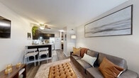 This 450 square foot apartment in Wilmington, NC, offers a well-designed living space with two bedrooms and one bathroom. The single-story layout maximizes efficiency, featuring a modern kitchen, comfortable living room, and a primary bedroom of 160 square feet.

The living area showcases a contemporary aesthetic with a leather sofa, decorative pillows, and a large abstract artwork. Natural light floods the space through windows adorned with sheer curtains. The kitchen boasts dark cabinetry contrasting with white appliances and light countertops, creating a sleek look. A small office nook adjacent to the kitchen provides a dedicated workspace.

Both bedrooms feature plush carpeting and ample natural light. The primary bedroom is adorned with blue accents, including a knitted throw and curtains, creating a serene atmosphere. Throughout the apartment, wood-look flooring adds warmth and continuity.

The thoughtful design incorporates storage solutions and decorative elements like potted plants and wall art, enhancing the overall ambiance. Despite its compact size, the apartment offers a harmonious blend of style, comfort, and functionality, making efficient use of every square foot.