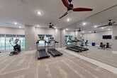 Located at 3904 Durham Park Rd in Stone Mountain, Georgia, this fitness center offers a thoughtfully designed workout space within a compact, single-floor footprint. The interior is finished with neutral gray walls, white baseboards, and durable patterned carpet tiles that lend a clean, modern aesthetic throughout.

The main exercise area is anchored by multiple treadmills and an elliptical trainer, positioned along a wall of large windows that invite natural light and views of the surrounding greenery. A full-length wall of floor-to-ceiling mirrors visually expands the space while allowing users to monitor their form during workouts. Two ceiling fans with dark wood-tone blades are mounted overhead, providing consistent air circulation.

A dedicated free weights and strength training zone includes a weight bench, color-coded medicine balls, and a cable resistance machine, all neatly organized. A wall-mounted flat-screen television provides entertainment during workouts. A stationary bike rounds out the cardio offerings.

Near the entrance, a posted fitness center rules board and a hand sanitizer dispenser reflect attention to cleanliness and safety. The entry area also features a rack of medicine balls and leads to an adjacent corridor. Recessed lighting throughout ensures the space is consistently well-lit, creating a functional and welcoming environment for residents to maintain an active lifestyle.