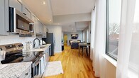 Located on State Street in Schenectady, NY, this well-designed one-bedroom, one-bathroom unit offers a thoughtfully organized single-floor layout that maximizes every square foot. Warm hardwood flooring runs throughout the main living areas, anchoring an open-concept design that seamlessly connects the kitchen, dining, and living spaces.

The kitchen is outfitted with gray cabinetry, granite countertops, a black matte faucet, and stainless steel appliances including a refrigerator, range, and dishwasher. Recessed lighting illuminates the space, which opens directly into the dining area and living room. Large street-facing windows bathe the main living area in natural light while offering views of the surrounding Schenectady streetscape.

The bedroom features plush carpeting, a double-door closet, angled ceiling details, and its own set of generous windows that continue the theme of natural light. The bathroom is finished with white tile flooring, a granite-topped vanity with gray cabinetry, a black matte faucet, a framed mirror, and a glass-enclosed shower. A dedicated laundry area houses a stacked washer and dryer unit for added convenience. The layout also accommodates a hallway and a workspace nook, rounding out this functional and modern urban residence.