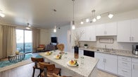 This single-floor residence offers a thoughtfully designed open-concept layout that seamlessly connects the kitchen, dining, and living areas. The kitchen is a standout feature, showcasing crisp white cabinetry, granite countertops, and a generously sized island with bar seating — ideal for casual dining. A full suite of appliances, including a stainless steel refrigerator, electric range, microwave, and dishwasher, completes the space. Track and pendant lighting add a polished touch overhead, while wood-look flooring runs throughout the main living areas.

The living room is warm and inviting, with a ceiling fan, sliding glass doors that open to a private outdoor patio, and ample space for comfortable seating arrangements. Two bedrooms offer ceiling fans, natural light through large windows with blinds and draping, and plush carpeting. The primary bedroom includes a walk-in closet for added storage convenience.

Both bathrooms feature wood-look flooring, white vanity cabinetry, and clean, bright finishes. One bathroom includes a tub-shower combination, while the second offers a spacious vanity with a large mirror. The overall ambiance of the residence is modern and welcoming, with a neutral palette that provides a versatile backdrop throughout.