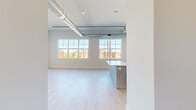 This single-floor unit blends modern design with industrial-chic character to create a bright, open living environment. Throughout the space, light hardwood flooring provides a clean, cohesive foundation, while exposed silver ductwork running along the ceiling adds a distinctive urban aesthetic. Elevated ceilings amplify the sense of spaciousness across all areas.

The open living and dining areas are defined by expansive multi-pane windows that flood the rooms with natural light and offer views of the surrounding neighborhood. A track lighting system along the ceiling provides additional flexibility for illumination.

The kitchen is a standout feature, outfitted with two-tone cabinetry — warm wood-grain lower cabinets paired with sleek white upper cabinets — and a white quartz countertop island that serves as both a workspace and gathering point. Stainless steel appliances, including a refrigerator with ice and water dispenser, range, microwave, and dishwasher, complete the well-appointed kitchen.

The bedrooms are generously sized, each benefiting from large windows that invite natural light and outdoor views. The bathroom is finished with striking marble-look porcelain tile covering both the floor and the full tub surround, lending a refined, upscale feel. Overall, this space delivers a seamless fusion of contemporary finishes and industrial design elements.