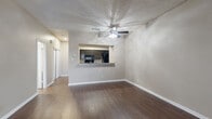 This two-floor residence offers a well-organized layout with distinct living and sleeping zones spread across both levels. The main floor features rich, dark hardwood-style flooring throughout the open living and dining areas, anchored by a classic wood-burning fireplace with a dark surround and a ceiling fan overhead. A pass-through countertop connects the living area to the kitchen, which is appointed with dark cabinetry, granite-style countertops, black appliances including a range, microwave, and refrigerator, and matching dark hardwood-style flooring. A textured ceiling is found throughout the main level. A staircase with a white-painted banister and handrail leads to the upper floor, where plush carpeting runs through the hallway and bedrooms. The bedrooms are generously sized, each featuring ceiling fans, window blinds allowing natural light, and closet storage. One bedroom includes sliding glass door access to the outdoors. The bathrooms feature granite-style countertops with undermount sinks, dark cabinetry, large mirrors, and a tub-shower combination with floor-to-ceiling stone-look tile. Neutral warm-toned walls and textured finishes carry throughout the space, creating a cohesive and comfortable atmosphere across all rooms.