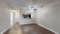 This two-floor residence offers a well-organized layout with distinct living and sleeping zones spread across both levels. The main floor features rich, dark hardwood-style flooring throughout the open living and dining areas, anchored by a classic wood-burning fireplace with a dark surround and a ceiling fan overhead. A pass-through countertop connects the living area to the kitchen, which is appointed with dark cabinetry, granite-style countertops, black appliances including a range, microwave, and refrigerator, and matching dark hardwood-style flooring. A textured ceiling is found throughout the main level. A staircase with a white-painted banister and handrail leads to the upper floor, where plush carpeting runs through the hallway and bedrooms. The bedrooms are generously sized, each featuring ceiling fans, window blinds allowing natural light, and closet storage. One bedroom includes sliding glass door access to the outdoors. The bathrooms feature granite-style countertops with undermount sinks, dark cabinetry, large mirrors, and a tub-shower combination with floor-to-ceiling stone-look tile. Neutral warm-toned walls and textured finishes carry throughout the space, creating a cohesive and comfortable atmosphere across all rooms.