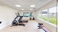 Located at 1850 Paisley Place in New Castle, Delaware, this dedicated exercise room offers a clean, functional environment designed for fitness. The space features light hardwood-style flooring and crisp white walls that create a bright, energizing atmosphere. A drop ceiling with recessed panel lighting ensures consistent, even illumination throughout the room.

Large windows along multiple walls allow generous natural light to fill the space and provide pleasant views of the surrounding green lawn and trees, making workouts feel open and connected to the outdoors. A wall-mounted television adds an entertainment option for those exercising.

The room is well-appointed with a comprehensive selection of fitness equipment, including two treadmills, an elliptical cross-trainer, a stationary upright bike, a multi-function cable strength training machine with a weight bench, and an abdominal bench. This variety supports a full range of cardiovascular and strength training workouts. The light, neutral color palette and uncluttered layout contribute to a focused and motivating exercise environment. Overall, this exercise room delivers a practical, fully outfitted fitness space suitable for a thorough daily workout routine.