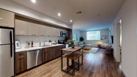 Located on Wilshire Boulevard in the heart of Los Angeles, this single-floor residence offers a thoughtfully designed open-concept layout with contemporary finishes. The kitchen is a standout feature, outfitted with a full suite of stainless steel appliances — including a refrigerator, electric range, microwave, and dishwasher — complemented by two-tone cabinetry in taupe and rich walnut, white countertops, and warm wood-look flooring that flows seamlessly throughout the living areas. A compact dining table with industrial-style stools provides a casual eating space just steps from the kitchen. The living room is bright and welcoming, benefiting from large windows that invite natural light and offer an open feel. A sectional sofa, glass-top coffee table, and decorative gold-framed mirror wall accent complete the space. The bedroom features plush carpeting, generous built-in closet storage, and sliding glass doors that open to a private balcony — an ideal retreat for enjoying outdoor views. The bathroom is finished with wood-look tile surround, a soaking tub, and clean white fixtures, contributing to the overall calm and modern aesthetic. This residence combines functional urban living with stylish, contemporary design in a prime Los Angeles location.