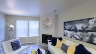 This single-floor residence offers a thoughtfully designed living space that balances comfort and style. The living room serves as the heart of the home, anchored by a sleek fireplace that adds warmth and a focal point to the room. Large windows dressed with vertical blinds allow generous natural light to pour in, brightening the neutral-toned walls and enhancing the open, airy feel of the space. Hardwood flooring runs throughout, adding a warm and polished foundation that complements the contemporary aesthetic. The living area is well-proportioned, providing ample room for relaxed seating arrangements. A striking sunburst wall sculpture adds an artistic touch above the fireplace, while bold monochromatic wall art contributes a modern, gallery-like quality to the room. The overall ambiance is clean and contemporary, with a neutral color palette accented by pops of yellow and navy that bring energy and personality to the space. The layout flows naturally, making the residence feel cohesive and welcoming from the moment you step inside.