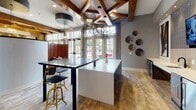 Located at 5426 Main St in Spring Hill, Tennessee, this single-story clubhouse delivers a well-appointed, contemporary interior designed to serve as a central gathering hub. The entry area makes an immediate impression with its soaring vaulted ceilings, large-format travertine-style tile flooring, and a striking combination of stacked stone and horizontally striped wood accent walls. A curved reception desk anchors the lobby, which is bathed in natural light through floor-to-ceiling French doors and oversized windows.

The lounge area features dramatic double-height windows dressed with sheer floor-length drapes, flooding the space with daylight. Comfortable seating arrangements, a wall-mounted television, and a mosaic tile feature wall with floating shelves create an inviting retreat. Adjacent to the lounge, the social gathering space showcases exposed wooden ceiling beams, bold pendant lighting, high-top seating with metallic bar stools, and a central island with a sleek white countertop.

A dedicated kitchenette/bar area runs along one wall, outfitted with stainless steel appliances, a wine refrigerator, a wet bar sink, white subway tile backsplash, and warm wood cabinetry beneath a wall-mounted display screen. Private rooms branching off the main areas provide quieter settings for focused work or meetings, completing a versatile and polished communal environment.