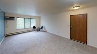 Located at 1103 Michigan Ave E in Battle Creek, Michigan, this single-floor unit offers a practical and comfortable layout with well-defined living spaces throughout. The living room is generously sized, featuring neutral carpet flooring, a textured ceiling, a large window with vertical blinds that allows ample natural light, and a baseboard heating system. An open sightline connects the living area to the kitchen, which is designed in a galley style with white cabinetry accented by warm wood trim, a double-basin sink, white appliances including a range, refrigerator, and built-in microwave, and durable tile-pattern flooring. Two carpeted bedrooms each feature ceiling fans with integrated lighting, windows with vertical blinds, and baseboard heating, providing a quiet and comfortable retreat. Closet access is available in the bedroom area, with warm wood-toned doors adding a classic touch throughout the unit. The bathroom includes a tub and shower combination with a striped curtain, a vanity with sink, a toilet, and tile-pattern flooring. The overall aesthetic is clean and neutral, offering a move-in ready canvas suitable for a variety of personal styles.