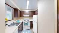 Located at 111 College Hill St in Cheney, WA, this single-floor unit offers three bedrooms, two bathrooms, and a practical layout designed for comfortable everyday living. The kitchen features rich dark brown cabinetry, ample upper and lower storage, light countertops, and a full suite of white appliances including an electric range, refrigerator, and dishwasher, all illuminated by overhead fluorescent lighting and complemented by light wood-look flooring. The living area transitions between carpet and wood-look flooring, with a ceiling fan overhead and a textured ceiling, offering a versatile and open feel. The generously sized primary bedroom includes a sliding door closet with built-in shelving and access to additional rooms, while the other bedrooms feature plush carpeting, large windows with vertical blinds, and baseboard heating units for efficient climate control. The bathrooms are well-appointed, with one featuring a dual-sink vanity with dark cabinetry, light countertops, a large mirror, and a separate tiled tub/shower combination with decorative white tilework. A hallway and closet provide additional storage and circulation throughout the unit. Neutral wall tones and consistent finishes create a cohesive, move-in-ready atmosphere throughout the home.