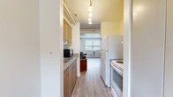 Located at 210 Lake St in Ithaca, NY, this three-bedroom, two-bathroom residence offers a well-organized single-floor layout designed to maximize functionality within a compact footprint. The galley-style kitchen features warm wood cabinetry, granite-look countertops, a double stainless steel sink, and full appliances including a refrigerator and range, all illuminated by pendant track lighting overhead. The kitchen opens toward a living area brightened by a window that brings in natural light. The three bedrooms are thoughtfully arranged throughout the unit, each featuring light wood-style flooring, neutral walls, and windows that allow daylight and outdoor views. The primary bedroom offers additional space and storage, while the secondary bedrooms are well-suited as private retreats or home offices. One bedroom displays painted cinder block accent walls, lending an urban, utilitarian character. The two bathrooms are cleanly appointed, with one featuring a full tub-shower combination and tile flooring. A connecting hallway ties the rooms together efficiently. The overall aesthetic is clean and functional, with consistent light-toned finishes throughout that create a bright and cohesive living environment.