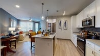 This single-floor residence offers a thoughtfully designed open-concept layout that seamlessly connects the kitchen, dining, and living areas. The kitchen is outfitted with crisp white shaker cabinetry, stainless steel appliances, a dark tile backsplash, light wood-style flooring, and a central island with pendant lighting — ideal for both casual dining and entertaining. The living room features a deep navy accent wall, ceiling fan, large windows with blinds, and access to an outdoor balcony, allowing for abundant natural light and a comfortable, inviting atmosphere.

The primary bedroom is a standout space, distinguished by a bold burnt-orange accent wall, plush carpeting, a ceiling fan, and direct balcony access. It includes a walk-in closet for generous storage. A second bedroom offers carpeted flooring, natural light from large windows, and a relaxed, versatile layout suitable for guests or a home office.

The bathroom is elegantly finished with large-format marble-look tile flooring, a glass-enclosed walk-in shower with matching tile surround, a single vanity with white cabinetry, and polished nickel fixtures. Consistent use of warm accent colors and contemporary decor throughout the space creates a cohesive and modern residential aesthetic.