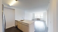 Located at One Third Avenue in Mineola, New York, this modern residence offers a thoughtfully designed single-floor layout with clean lines and a bright, contemporary aesthetic throughout. The open-concept living and kitchen area serves as the heart of the home, where rich dark hardwood flooring contrasts elegantly with crisp white walls and ceilings. A central kitchen island with a light quartz countertop and undermount sink anchors the space, providing both functionality and a natural gathering point. The kitchen is fully equipped with stainless steel appliances, including a French door refrigerator with ice maker, gas range, built-in microwave, and dishwasher, all complemented by warm-toned cabinetry and ample upper storage. The living area is generously proportioned, bathed in natural light from large windows that frame views of the surrounding neighborhood. The bedroom is a calm, well-sized retreat featuring the same hardwood flooring and a window with a roller shade for privacy. The bathroom is finished with textured tile walls, a stone-topped vanity, and a large mirror. A dedicated closet housing a stacked washer and dryer adds everyday convenience, completing this well-appointed urban residence.