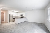 Located at 1 Mirror Lane in Moriches, NY, this two-floor home offers a clean, neutral aesthetic throughout its well-organized layout. The main level features a kitchen equipped with stainless steel appliances, including a refrigerator, range, and built-in microwave, all set against white cabinetry with ample storage. A peninsula countertop with a neutral laminate surface separates the kitchen from the adjoining carpeted living area, creating an open, connected feel. The living space is bright and generously sized, with sliding glass doors that frame views of the surrounding greenery and allow abundant natural light to fill the room. An additional window with blinds further enhances the airy atmosphere. Entry areas transition between tile flooring and carpet, clearly delineating functional zones. A closet with wire shelving provides convenient storage near the living area. Bathrooms on both levels feature white fixtures, a tub-shower combination with sliding glass doors, mirrored medicine cabinets, and vanity sinks. The upper level, accessible via a staircase with a wood railing, includes carpeted bedrooms with windows overlooking the wooded surroundings, offering a quiet, comfortable retreat.