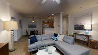 Located at 111 Springview Lane in Summerville, South Carolina, this single-floor residence offers a thoughtfully designed open-concept layout that seamlessly connects the main living areas. The living room serves as the heart of the home, featuring a ceiling fan with light fixture and recessed lighting that provide both comfort and illumination. A spacious sectional sofa arrangement anchors the space, complemented by a light-toned carpet that adds warmth underfoot. A decorative column adds an architectural accent, subtly defining the transition between the living and dining areas. The dining area is positioned adjacent to the living space, featuring a pendant light fixture overhead and a cozy table and chair set — ideal for everyday meals or intimate gatherings. The kitchen, visible from the main living area, offers warm wood cabinetry, tile countertops, and standard appliances, including a microwave. A pass-through or open partition keeps the kitchen connected to the rest of the living space, promoting a sociable and airy atmosphere. The overall ambiance is casual yet polished, with neutral tones throughout that create a calm, inviting environment well-suited to comfortable everyday living in this Summerville community.