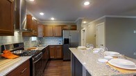 This kitchen is thoughtfully designed to balance functionality with an inviting aesthetic. The space is anchored by a expansive granite-topped island that doubles as a dining and entertaining area, currently set with glassware and place settings, highlighting its versatility. Rich, dark hardwood flooring runs throughout, contrasting beautifully with the warm honey-toned wood cabinetry that lines the walls and provides generous storage. The cabinetry features classic raised-panel doors with brushed hardware, complemented by crown molding that adds a refined, finished look along the upper perimeter. A subway tile backsplash in a soft grey-green hue adds texture and visual interest behind the cooktop and sink areas. Stainless steel appliances include a large French door refrigerator with an in-door ice and water dispenser, a gas range with multiple burners, and an integrated range hood. Recessed lighting is evenly distributed across the ceiling, ensuring the workspace is well-lit throughout. Crown molding trims the ceiling, enhancing the overall polished character of the room. The open layout allows for easy movement between prep, cooking, and serving areas.