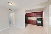 Located at 115 SW 16th St in Pompano Beach, Florida, this two-bedroom, one-bathroom single-floor unit offers a practical and well-organized layout. Light-toned tile flooring runs consistently throughout the entire space, contributing to a clean, cohesive look.

The combined living and dining area greets you upon entry, flanked by two windows that allow natural light to fill the room. The open layout provides a comfortable flow into the kitchen, which is separated by a half-wall partition. The kitchen is outfitted with rich, dark mahogany-toned cabinetry extending from floor to ceiling, complemented by a warm stone-patterned tile backsplash, a built-in sink, and black appliances including a range and refrigerator.

A hallway connects the main living area to the two bedrooms, each featuring neutral walls, tile flooring, and individual closets with bifold doors. The primary bedroom is a well-proportioned space with ample room for furnishings. The shared full bathroom includes a tub-shower combination with white subway tile surround.

The unit features textured ceilings throughout, and ceiling-mounted HVAC vents ensure year-round climate comfort — an essential in South Florida's warm climate. The layout is efficient and functional, making effective use of the available space.