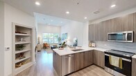 Located at 80 Mill Street in Hanover, MA, this thoughtfully designed one-bedroom, two-bathroom residence offers a refined modern aesthetic across a single floor. The open-concept kitchen and living area serves as the heart of the home, where the kitchen showcases sleek flat-panel cabinetry in a warm wood-grain finish, white quartz countertops, a classic tile backsplash, and a full suite of stainless steel Whirlpool appliances. The adjacent living room features soaring ceilings, light wood-style flooring, and generous windows that fill the space with natural light and outdoor views. A built-in shelving nook near the entry provides both functional storage and a welcoming focal point. The bedroom is carpeted and equally bright, with large windows and elevated ceilings that lend a sense of spaciousness. The primary bathroom impresses with large-format marble-look tile flooring, a dual-sink vanity with wood-tone cabinetry, and a wide illuminated mirror. The second bathroom offers a soaking tub enclosed by marble-look tile surround with brushed nickel fixtures. A dedicated closet completes the layout, and the overall palette of soft whites, warm woods, and brushed metals creates a cohesive, contemporary ambiance throughout.