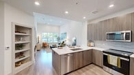 Located at 80 Mill Street in Hanover, MA, this thoughtfully designed one-bedroom, two-bathroom residence offers a refined modern aesthetic across a single floor. The open-concept kitchen and living area serves as the heart of the home, where the kitchen showcases sleek flat-panel cabinetry in a warm wood-grain finish, white quartz countertops, a classic tile backsplash, and a full suite of stainless steel Whirlpool appliances. The adjacent living room features soaring ceilings, light wood-style flooring, and generous windows that fill the space with natural light and outdoor views. A built-in shelving nook near the entry provides both functional storage and a welcoming focal point. The bedroom is carpeted and equally bright, with large windows and elevated ceilings that lend a sense of spaciousness. The primary bathroom impresses with large-format marble-look tile flooring, a dual-sink vanity with wood-tone cabinetry, and a wide illuminated mirror. The second bathroom offers a soaking tub enclosed by marble-look tile surround with brushed nickel fixtures. A dedicated closet completes the layout, and the overall palette of soft whites, warm woods, and brushed metals creates a cohesive, contemporary ambiance throughout.