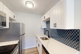 Located at 3009 W 13 Mile Rd in Royal Oak, MI, this thoughtfully updated 2-bedroom, 1-bathroom unit offers a clean, modern aesthetic throughout its single-floor layout. The galley-style kitchen is a standout feature, showcasing crisp white shaker cabinets with matte black hardware, sleek quartz countertops with marble-like veining, a navy arabesque tile backsplash, and a full suite of stainless steel appliances including a refrigerator, electric range, microwave, and dishwasher. Light wood-tone flooring ties the kitchen seamlessly into the open dining and living areas, which offer a bright, airy feel with neutral walls and generous space for entertaining or relaxing. A central hallway connects the main living areas to the bedrooms and bathroom. The spacious primary bedroom features plush carpeting, a wide closet with bifold doors, and ample room to furnish comfortably. The second bedroom also offers wood-look flooring, natural light from a window, and baseboard heating. The full bathroom is finished in a clean, modern style with white cabinetry, quartz countertops, matte black accents, and wood-tone flooring. Three closets throughout the unit provide excellent storage. The overall ambiance is fresh, updated, and move-in ready.