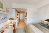 Located at 50 Western Avenue in Boston's Allston neighborhood, this thoughtfully designed studio offers a smart, efficient layout that maximizes every square foot. Light wood-tone flooring runs throughout, complementing a bright, white interior that creates a clean and airy atmosphere.

The open-concept living space seamlessly integrates the kitchen, dining, and sleeping areas. The modern kitchen features sleek white cabinetry extending to the ceiling, white quartz countertops, and a full suite of stainless steel appliances including a refrigerator, range, over-the-range microwave, and dishwasher. A peninsula counter provides additional workspace and casual dining possibilities.

The sleeping area is defined by a patterned accent wall in a subtle herringbone design, adding texture and visual interest. Large windows allow natural light to pour in, offering views of the surrounding Boston cityscape. A dedicated desk area provides a functional workspace within the living zone.

The bathroom features light wood-toned cabinetry, a white sink vanity, and a rounded mirror, maintaining the warm, modern aesthetic found throughout the unit. Additional conveniences include an in-unit laundry area and a closet, ensuring practical storage solutions. This studio is an ideal option for those seeking a well-appointed, efficiently organized living space in Boston.