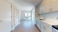 This well-designed single-floor unit offers a clean, contemporary aesthetic throughout, with light-toned hardwood flooring and a crisp white palette that create a bright and airy atmosphere. The open-concept layout connects the kitchen and living area seamlessly, maximizing the sense of space and encouraging an easy flow between zones.

The kitchen is fully equipped with stainless steel appliances, including a French door refrigerator, electric range, built-in microwave, and dishwasher. Sleek gray cabinetry with bar-pull hardware extends from floor to ceiling, providing ample storage, while white countertops and a tile backsplash contribute to the kitchen's modern, polished look.

The living area is generously proportioned, bathed in natural light from a large window that frames an impressive urban skyline. A wall-mounted HVAC unit ensures year-round comfort. A louvered closet door adds a practical and stylish storage element to the space.

The bedroom is a tranquil retreat, benefiting from expansive windows and a glass sliding door that offer sweeping city views and abundant natural light. The neutral tones and hardwood flooring continue seamlessly from the main living area.

The bathroom features clean white subway tile surrounding a full soaking tub and shower combination, complemented by taupe floor tiles and chrome fixtures, resulting in a simple yet refined finish throughout.