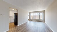 This single-floor unit offers a practical and comfortable layout with a clear separation between living, sleeping, and functional spaces. The open living area is a standout feature, finished with light wood-look vinyl plank flooring and neutral-toned walls that create a bright, airy atmosphere. A large picture window along one wall floods the space with natural light while providing outdoor views, and baseboard heating runs beneath the sill for efficient climate control. A textured ceiling adds a subtle design element throughout the main living zone.

The kitchen is well-equipped, featuring white shaker-style cabinetry with brushed nickel hardware, granite-look countertops, a double-basin sink, and black stainless appliances including a refrigerator and electric range with a ventilation hood. Wood-look flooring continues throughout the kitchen, which connects conveniently to the rest of the unit.

The bedrooms are carpeted for comfort and include windows with blinds, ceiling fans, and baseboard heating. The bathroom is cleanly finished with white tile, a full soaking tub with shower, and classic fixtures. An entry area with a closet completes the functional layout of this well-maintained space.