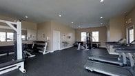 This fitness center offers a clean, functional environment purpose-built for exercise and physical wellness. The space features durable dark rubber flooring throughout, providing a safe and resilient surface suited to a wide variety of workouts. Recessed lighting in the smooth ceiling ensures the room is well-lit, complemented by natural light streaming in through windows along the far wall.

The room is thoughtfully arranged with a diverse selection of equipment. A tiered dumbbell rack lines one wall, stocked with a full range of free weights for strength training. A multi-station cable machine occupies a central position, offering versatility for resistance-based exercises. A SportsArt treadmill is prominently positioned for cardiovascular training, and additional equipment such as a weight bench and stability ball rounds out the offerings.

Motivational wall lettering adds an energizing touch to the neutral beige walls, fostering a focused workout atmosphere. A water fountain is conveniently located near the entry door, ensuring easy access to hydration. The overall layout is open and uncluttered, allowing ample space for movement and exercise. This fitness center is well-suited for a comprehensive training regimen in a comfortable, organized setting.