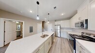 This two-story residence in Metuchen, NJ offers a well-designed layout across two floors, totaling over 1,300 square feet of living space. The main floor is anchored by an open-concept kitchen and living area, where a large central island with a quartz countertop and undermount sink serves as the focal point. Pendant lighting illuminates the island, while crisp white shaker-style cabinetry, stainless steel appliances — including a refrigerator, range, and microwave — and light wood-style flooring complete the modern aesthetic. The upper floor hosts both bedrooms and two full bathrooms. The generously sized primary bedroom impresses with soaring vaulted ceilings, a skylight that floods the room with natural light, and a window overlooking the surrounding neighborhood. The second bedroom features large windows with views of the outdoors, providing a bright and airy atmosphere. Both bedrooms include closet storage. The bathrooms are finished with clean, neutral tones, featuring tub-shower combinations and wood-style flooring. Throughout the home, a consistent warm neutral color palette, recessed lighting, and light hardwood-style floors create a cohesive, contemporary feel.