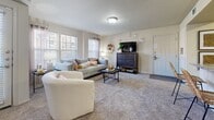 This single-floor residence offers a thoughtfully designed layout with a cohesive aesthetic defined by rich dark wood cabinetry, neutral tones, and plush carpeted living spaces. The kitchen is a functional highlight, featuring stainless steel appliances including a French door refrigerator with ice dispenser, an electric range with over-the-range microwave, and generous counter space with granite-look surfaces. Abundant dark wood cabinetry provides ample storage, while large-format tile flooring adds a polished finish. The open living area is bright and welcoming, with multiple windows dressed in blinds and sheer curtains that allow natural light to fill the room. Soft carpeting extends throughout the living and dining zones, creating a warm and comfortable atmosphere. The primary bedroom is a spacious retreat complete with a ceiling fan, plush carpet, and a walk-in closet. A second bedroom offers similar comfort with a ceiling fan, natural light, and ample storage. The bathroom is well-appointed with a dark wood vanity, granite-look countertop, a wide illuminated mirror with bar lighting above, and large-format tile flooring. A dedicated laundry area with washer and dryer connections adds practical convenience to this well-rounded residence.