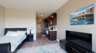 This single-floor studio unit offers a thoughtfully arranged open-concept layout that efficiently combines living, sleeping, and dining areas into one cohesive space. Light wood-tone flooring runs throughout, providing a clean and contemporary foundation that ties the entire unit together.

The kitchen is positioned along one wall and features rich, dark espresso cabinetry with modern hardware, light countertops, and a full suite of stainless steel appliances including a refrigerator, electric range, over-the-range microwave, and dishwasher. A compact peninsula provides additional counter space and a natural visual boundary between the kitchen and the main living area.

The living and sleeping area is open and versatile, accommodating both a bed and a seating area with ease. Large sliding glass doors lead to a private balcony, allowing generous natural light to fill the space while offering pleasant views of the surrounding greenery and neighborhood below. The neutral wall tones complement the warm cabinetry and flooring throughout.

The bathroom continues the dark cabinetry theme with a matching vanity topped with a white sink, a large mirror, and wood-look flooring that maintains the unit's cohesive aesthetic. Clean lines and efficient use of space make this unit a practical and comfortable single-floor residence.
