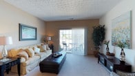 Located at 4333 Parkway Village Dr in Grove City, Ohio, this two-story residence offers a well-designed layout with a warm and inviting atmosphere. The living room serves as a central gathering space, featuring plush carpeting, neutral-toned walls, and a textured ceiling that adds character to the room. A large sliding glass door floods the space with natural light and provides direct access to an outdoor patio, where seating is visible beyond the vertical blinds — a seamless connection between interior comfort and outdoor relaxation. The living area is generously proportioned, easily accommodating a full sofa, an oversized ottoman, and additional furnishings without feeling crowded. A framed wall accent and a decorative potted plant add a finishing touch to the room's welcoming aesthetic. The two-floor layout of the home offers functional separation between living and private spaces, making it well-suited for a variety of lifestyle needs. Situated in Grove City, a community south of Columbus known for its suburban charm, this residence benefits from a peaceful neighborhood setting while maintaining convenient access to local amenities, shopping, and major roadways.