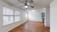 This two-floor residence offers a practical and comfortable layout designed for everyday living. The main living area is bright and open, featuring warm hardwood-style flooring that runs throughout much of the space, a textured ceiling, and a ceiling fan with integrated lighting. Large windows fitted with blinds allow natural light to fill the room, creating a welcoming atmosphere. The living area flows seamlessly into the galley-style kitchen, which is equipped with gray cabinetry, speckled laminate countertops, a tiled backsplash, a double-basin sink, and black appliances including a refrigerator, electric range, built-in microwave, and dishwasher — providing ample functionality for cooking and storage. The bedrooms continue the hardwood-style flooring in some rooms, while at least one bedroom features plush carpet, offering a softer feel. Each bedroom includes a ceiling fan and window for ventilation and natural light, with select rooms offering closet space. The bathroom is well-appointed with a wide vanity topped with speckled countertops, gray cabinetry, a large mirror, and a full tub-shower combo. Clean white walls and consistent finishes throughout the space contribute to a cohesive, move-in-ready aesthetic across both floors.