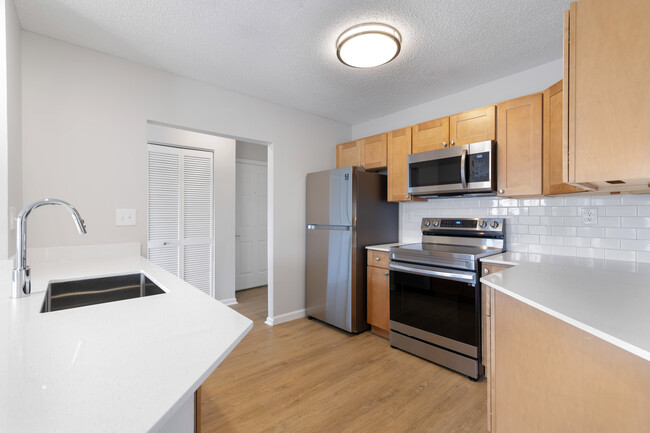 Renovated Package I kitchen with stainless steel appliances, white quartz countertops, maple cabinetry, white tile backsplash, and hard surface flooring - Avalon Burlington