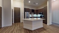 Located at 1300 Fourth Ave N in Nashville, Tennessee, this single-floor unit offers a well-designed, modern living space with quality finishes throughout. The open-concept kitchen serves as a central highlight, featuring rich dark cabinetry, a mosaic tile backsplash, stainless steel appliances including a French door refrigerator, built-in microwave, and range. A granite-topped kitchen island provides additional prep space and a natural gathering point, while wood-look flooring adds warmth and continuity across the main living area. A convenient coat hook station near the entry offers practical storage upon arrival. The bedroom is a calm, neutral retreat with plush carpeting and a window dressed with blinds that allow natural light to filter in, offering a view of the surrounding greenery. The bathroom is thoughtfully appointed with a granite-topped vanity, brushed nickel hardware, tile flooring, and a full tub-shower combination with white tile surround. Clean white walls and neutral tones throughout create a cohesive, move-in-ready aesthetic that is both functional and inviting for everyday living in the heart of Nashville.
