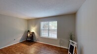 Located at 2201 Mossy Oaks Rd in Beaufort, South Carolina, this single-floor, 2-bedroom, 2-bathroom residence offers a practical and comfortable layout. The living room welcomes you with warm wood-look flooring, neutral gray walls, a textured ceiling, and a front entry door that fills the space with natural light. The kitchen is a standout feature, boasting crisp white cabinetry, dark granite countertops, a stainless steel dishwasher, and black appliances including a refrigerator and range — all set over matching wood-look flooring. Both bathrooms echo the kitchen's design with granite vanity tops and clean white fixtures, including a tiled tub-shower combination in one bath. The two bedrooms are finished with plush carpet, bright windows with blinds that frame views of surrounding greenery, and ceiling fans with integrated lighting for year-round comfort. A dedicated closet and hallway provide practical storage and circulation throughout the home. Neutral tones and consistent finishes create a cohesive, move-in-ready atmosphere suited for comfortable everyday living in the heart of Beaufort's Lowcountry setting.