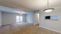 This single-floor residence offers a practical and comfortable layout across two bedrooms and two bathrooms. The open living area is finished with neutral-toned carpet and light gray walls, creating a bright and welcoming atmosphere. A ceiling fan anchors the main living space, which features a set of French doors that invite natural light and provide outdoor access. A step-down area adds subtle architectural interest to the living room, which flows seamlessly toward a pendant-lit dining space. The galley-style kitchen is efficiently designed with white cabinetry, gray laminate countertops, a stainless steel sink, light wood-look flooring, and black appliances, offering ample storage and counter space. Both bedrooms are carpeted and painted in warm neutral tones, with the primary bedroom benefiting from two windows that frame views of mature surrounding trees. The second bedroom features a single window with natural light. Each bathroom is clean and functional, featuring wood-look tile flooring, white vanity cabinetry, a large mirror with overhead lighting, and a tiled shower-tub combination. Two closets provide additional storage throughout the unit. The overall aesthetic is cohesive, practical, and move-in ready.