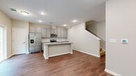 Located at 1018 Catalyst Blvd in Charlotte, NC, this two-story home offers three bedrooms and three full bathrooms spread across two well-proportioned floors. The main level features an open-concept kitchen and living area finished with warm hardwood-style flooring. The kitchen is well-appointed with gray cabinetry, granite countertops, a subway tile backsplash, stainless steel appliances including a side-by-side refrigerator, electric range, and built-in microwave, plus a central island with a sink. A staircase connects the main level to the upper floor, which houses all three bedrooms. The generously sized primary bedroom provides ample space and is outfitted with ceiling fan lighting. Additional bedrooms are carpeted and offer comfortable proportions with neutral tones throughout. The three full bathrooms are consistently finished with granite-topped gray vanities and wood-style flooring; one features a walk-in glass-door shower while another includes a full soaking tub. A dedicated laundry room on the upper level accommodates a full-size washer and dryer with overhead shelving. Natural light is present throughout, with windows offering views of the surrounding greenery.