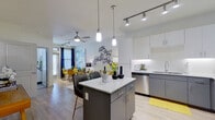 This thoughtfully designed 2-bedroom, 2-bathroom residence offers a contemporary open-concept layout that seamlessly connects the kitchen, dining, and living areas. The kitchen is a standout feature, showcasing two-tone cabinetry — white uppers paired with charcoal gray lowers — granite countertops, a subway tile backsplash, and a full suite of stainless steel appliances including a refrigerator, range, microwave, and dishwasher. A central island with seating provides additional prep space and casual dining. Light wood-style flooring flows throughout the main living areas, complemented by track lighting and pendant fixtures that enhance the bright, airy atmosphere. The living area is generously proportioned for its footprint, with room for a full seating arrangement and a dedicated dining nook bathed in natural light from large windows with patio door access. The primary bedroom features a walk-in closet and a ceiling fan, offering a comfortable private retreat. Both bathrooms are finished with granite-topped vanities, gray cabinetry, and marble-style tiled tub-shower surrounds. The overall design aesthetic is clean and modern, with consistent finishes throughout that create a cohesive and polished living environment.