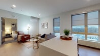 Located at 9150 W Watertown Plank Rd in Wauwatosa, Wisconsin, this modern single-floor residence offers a thoughtfully designed open-concept layout that seamlessly connects the living, dining, and kitchen areas. Light-toned hardwood flooring flows throughout, complementing the clean, neutral palette of the interior.

The living area is bright and welcoming, featuring large windows with roller shades that frame outdoor views and fill the space with natural light. A wall-mounted split HVAC unit provides efficient climate control. The kitchen is well-appointed with stainless steel Whirlpool appliances — including a range, microwave, dishwasher, and refrigerator — paired with wood-tone cabinetry, open shelving, and a white quartz-topped island with bar seating, ideal for casual dining.

The residence includes two bedrooms, each finished with soft carpeting, recessed lighting, and large windows. One bedroom features its own wall-mounted split unit for personalized comfort. A floor-to-ceiling wood-panel wardrobe provides generous storage along the hallway leading to the rooms.

A full bathroom and a dedicated in-unit laundry closet with a stacked washer and dryer round out the functional amenities. The overall ambiance is clean, contemporary, and comfortable, reflecting a modern residential aesthetic throughout.