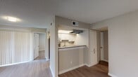 This single-floor residence is designed with a clean, neutral aesthetic throughout, utilizing warm beige tones, white trim, and wood-look flooring that flows consistently across every room. The living area serves as the central gathering space, highlighted by a white-mantled fireplace, a ceiling fan with integrated lighting, and windows fitted with blinds and vertical panel treatments that allow natural light to filter in. A sliding glass door provides additional access and light to the living space.

The kitchen is positioned adjacent to the living area and features a pass-through peninsula that opens toward the main living space, creating a connected feel. Inside, white shaker-style cabinetry lines the walls, complemented by dark countertops, stainless steel appliances including a refrigerator and range, an under-cabinet range hood, and a single-basin sink. Light wood-look flooring continues into this space.

The bedrooms are generously proportioned, each equipped with ceiling fans and windows that bring in natural light. The neutral walls and consistent flooring give each room a calm, versatile character.

Two bathrooms serve the residence, both featuring white vanity cabinetry with dark countertops, framed mirrors, and tub-shower combinations with white tile surrounds. The textured ceilings are present throughout the unit, adding a consistent architectural detail across all spaces.