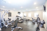 This fitness center is a comprehensively outfitted workout facility designed to support a full range of exercise routines. The space is spread across a single floor and features durable dark rubber flooring throughout, providing a safe and functional surface ideal for all types of physical activity.

The cardio section is well-stocked with multiple treadmills, an elliptical trainer, and a stationary recumbent bike, offering users a variety of aerobic workout options. Several windows along the walls allow natural light to fill the space, creating a bright and energizing atmosphere. Recessed lighting in the textured ceiling provides consistent illumination throughout.

The strength training area includes a multi-station cable machine along with a set of adjustable dumbbells neatly organized on tiered racks, accompanied by an adjustable workout bench for targeted exercises. Full-length wall mirrors are strategically placed to allow users to monitor their form during workouts. Wall-mounted flat-screen TVs are positioned in multiple areas of the room, keeping exercisers entertained during their sessions.

The clean, neutral-toned walls and organized layout contribute to a focused and professional gym environment. Fitness center rules are posted on the wall, and the space appears well-maintained, reflecting a commitment to providing a quality workout experience.