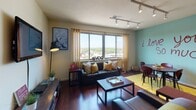 This lively single-floor residence offers a thoughtfully designed layout filled with personality and urban charm. The open-concept living and dining area is anchored by rich hardwood flooring and large windows that frame sweeping city and treetop views, flooding the space with natural light. Track lighting and a teal accent wall bearing a bold painted mural add a creative, eclectic character to the common area.

The kitchen is a standout, featuring warm yellow cabinetry, granite countertops, stainless steel appliances, and a peninsula with bar seating. A dramatic brick-tiled backsplash extending to the ceiling creates a striking focal point. The adjacent dining area comfortably accommodates a round wooden table and chairs.

The space includes two bedrooms, each with carpeted floors, ceiling fans, and ample natural light. One bedroom features a cozy, compact layout with a window view, while the second is more spacious and accented with decorative wall art and bold curtains.

Two full bathrooms are finished with tile flooring, tile-surround tub-shower combinations, granite-topped vanities, and wood cabinetry, offering a clean and functional design. Throughout the residence, the interplay of bold colors, eclectic décor, and practical finishes creates a warm and energetic living environment.